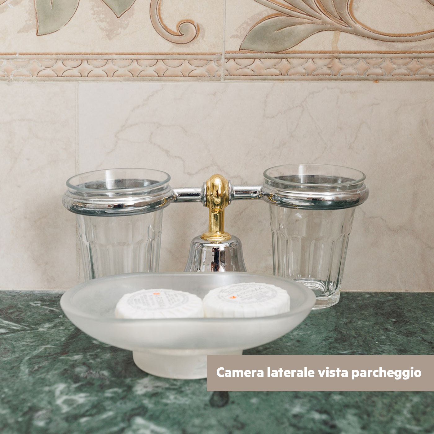 Dettaglio accessori bagno con bicchieri e sapone su marmo verde.