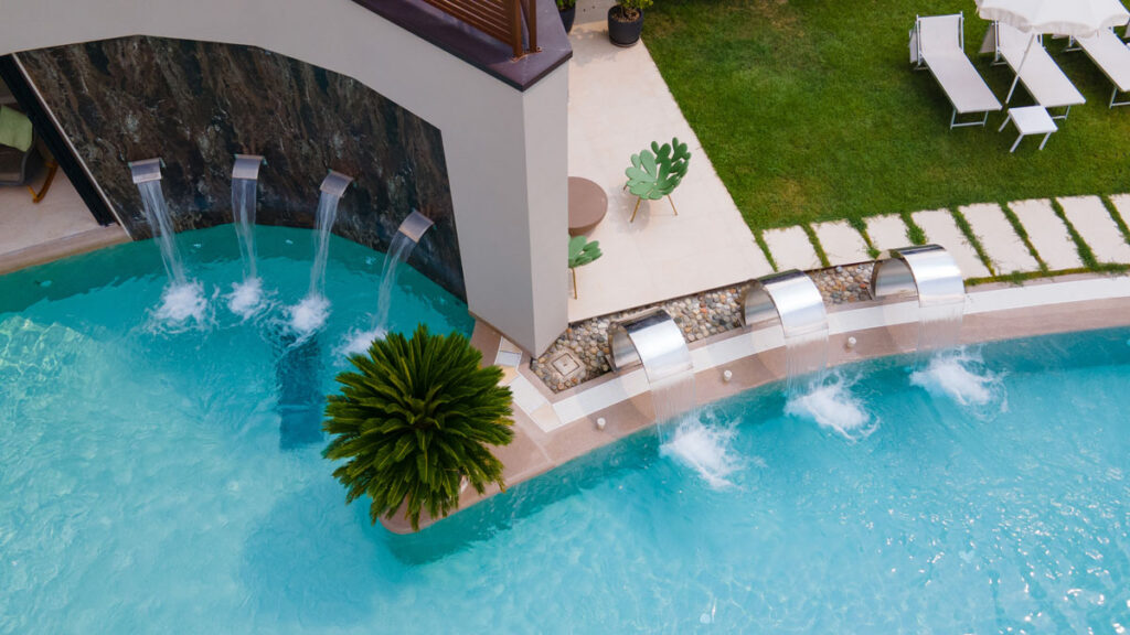 Vista panoramica della piscina esterna dell'hotel con fontane d'acqua e zona relax coperta.