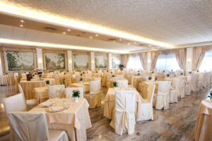 Sala ristorante elegante e luminosa con tavoli decorati, sedie raffinate e affreschi alle pareti.