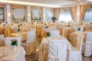Sala ristorante elegante e luminosa con tavoli decorati, sedie raffinate e affreschi alle pareti.