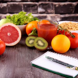 Frutta fresca, kiwi e pompelmo con succo di pomodoro, legumi e insalata su tavolo, dieta sana con taccuino per menu