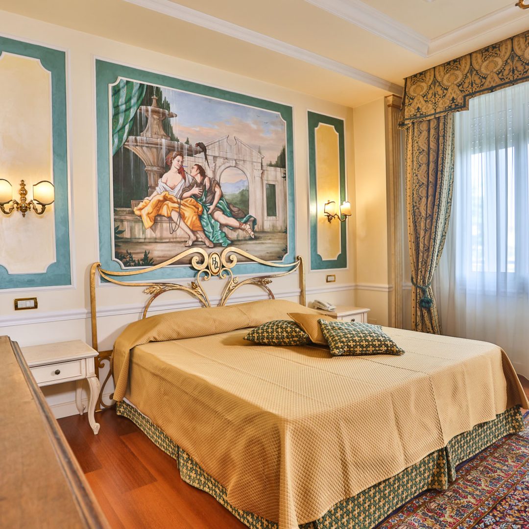 Camera da letto della Suite Atena con letto matrimoniale e affreschi artistici.