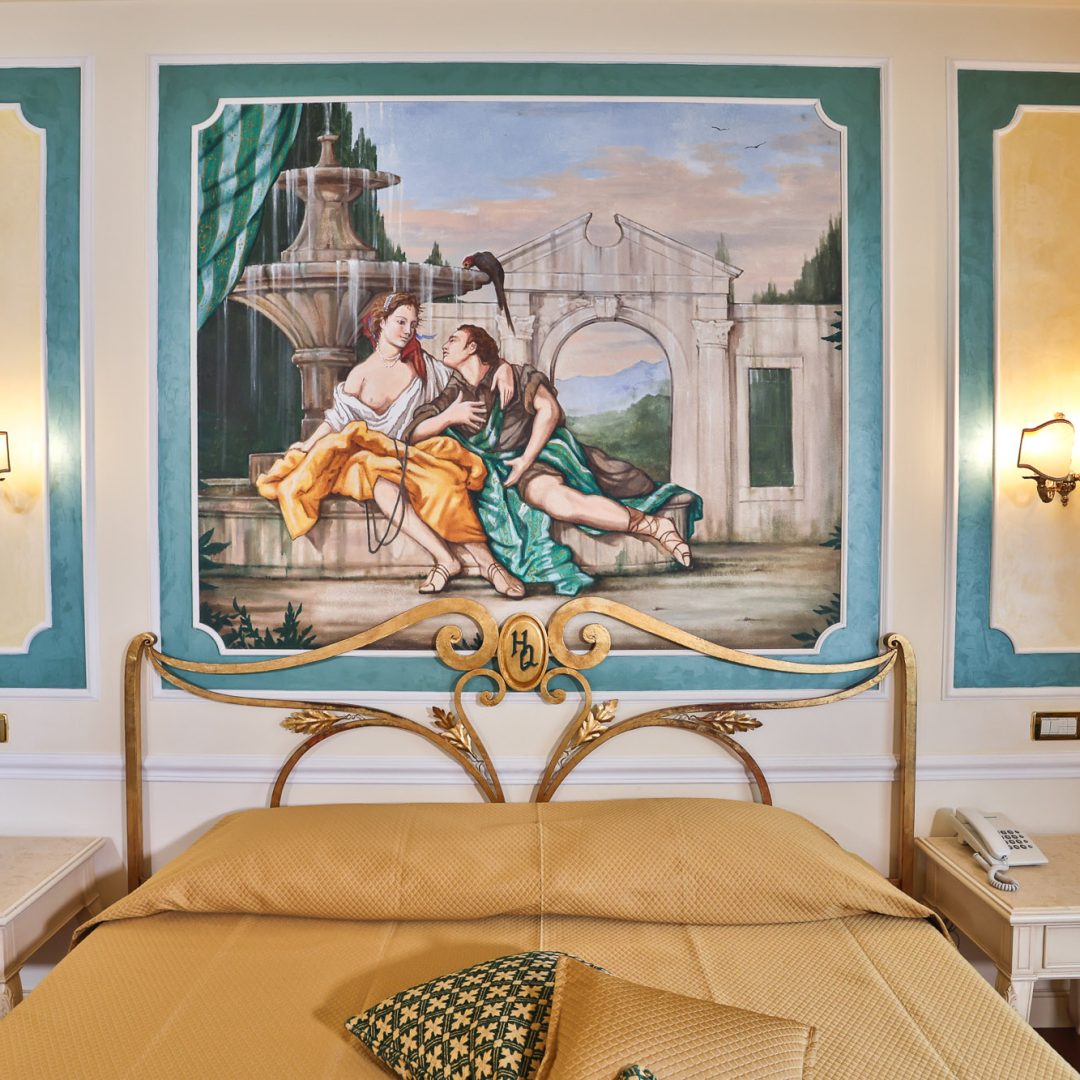 Camera da letto della Suite Atena con letto matrimoniale e affreschi artistici.