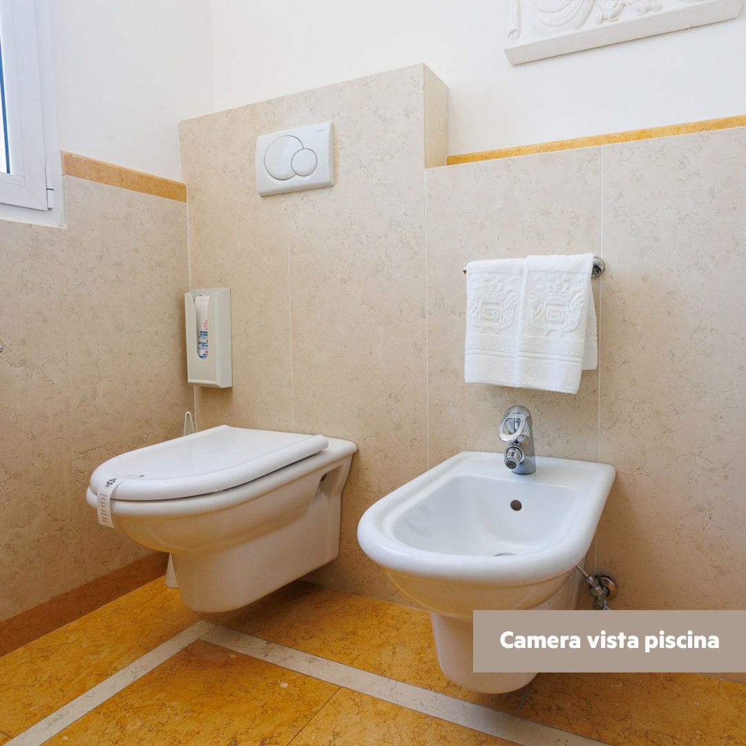 Bidet e WC in un bagno con piastrelle beige e marmo giallo.