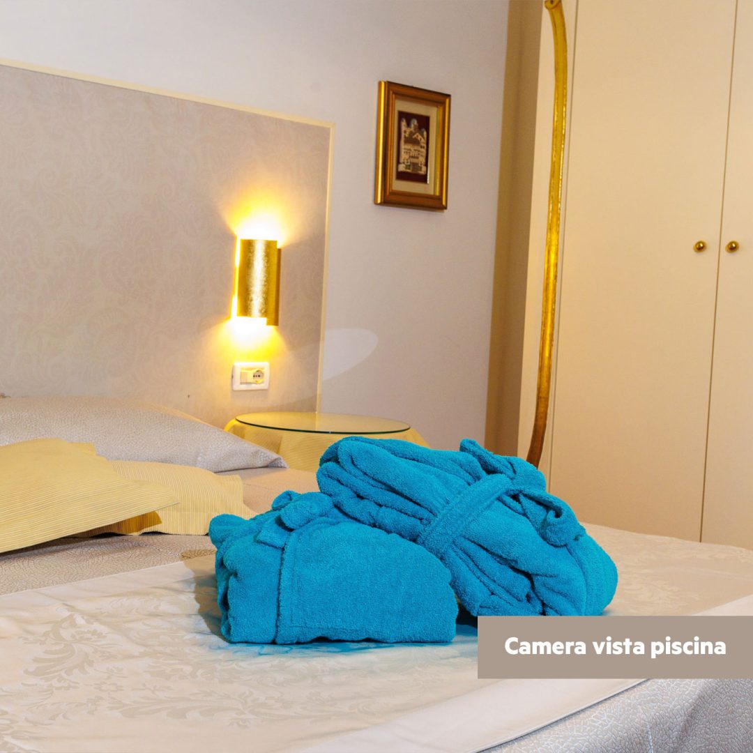 Letto matrimoniale con testata decorata in oro e biancheria bianca nella camera Superior lato piscina.