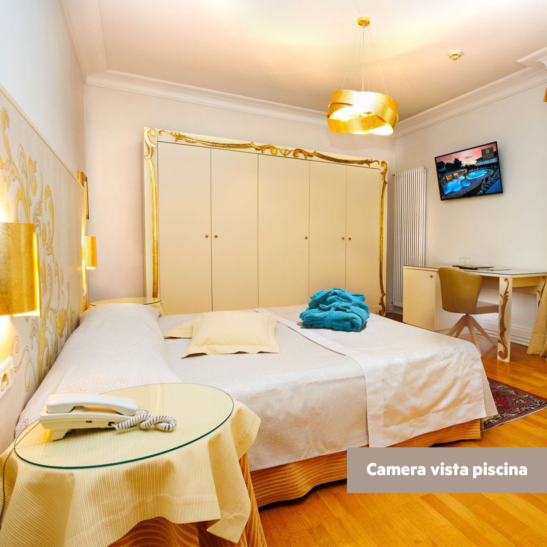 Vista laterale della camera Superior lato piscina con letto matrimoniale e finestra con tende dorate.